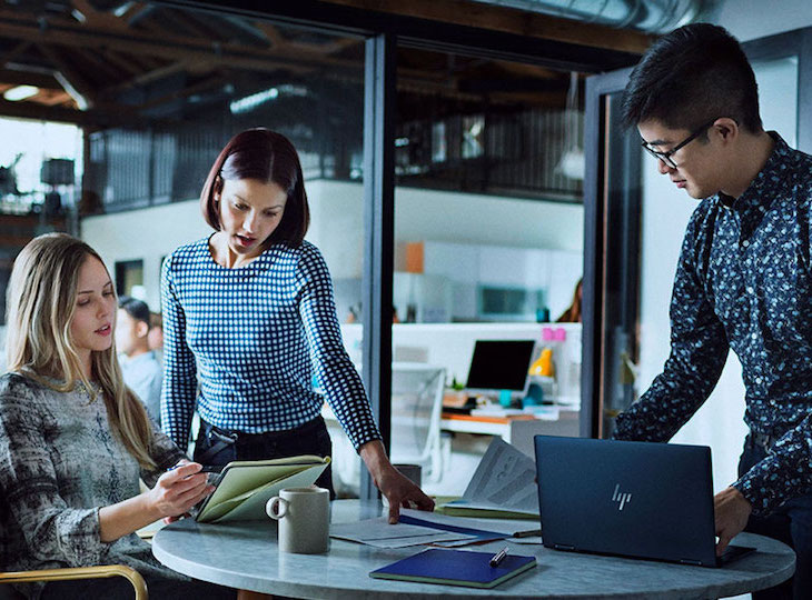 Colleagues communicating during the work process in the office sitting at a table with an HP laptop.