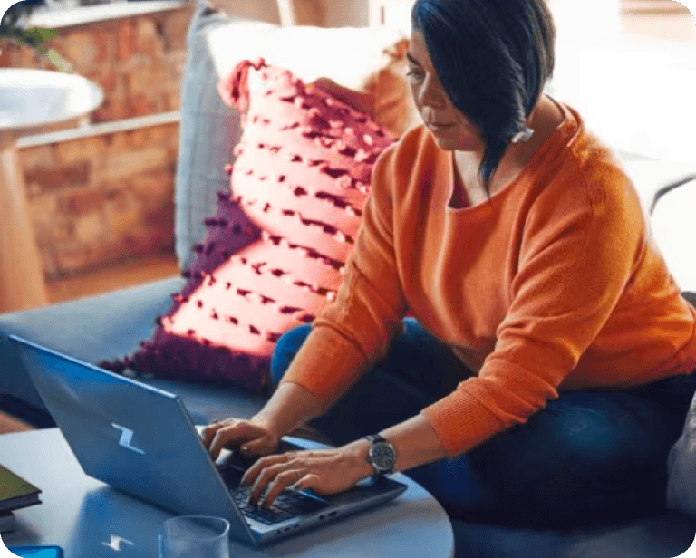 Seorang wanita di sofa sedang bekerja menggunakan laptop HP di atas meja kopi.