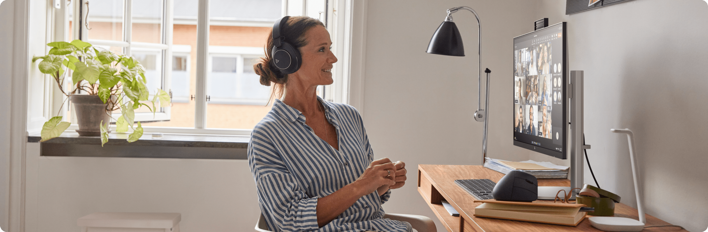 Professional sitting at a desk wearing headphones and participating in a video call on a desktop HP monitor with intelligent camera control and AI‑driven features like those offered by Poly Camera Pro.