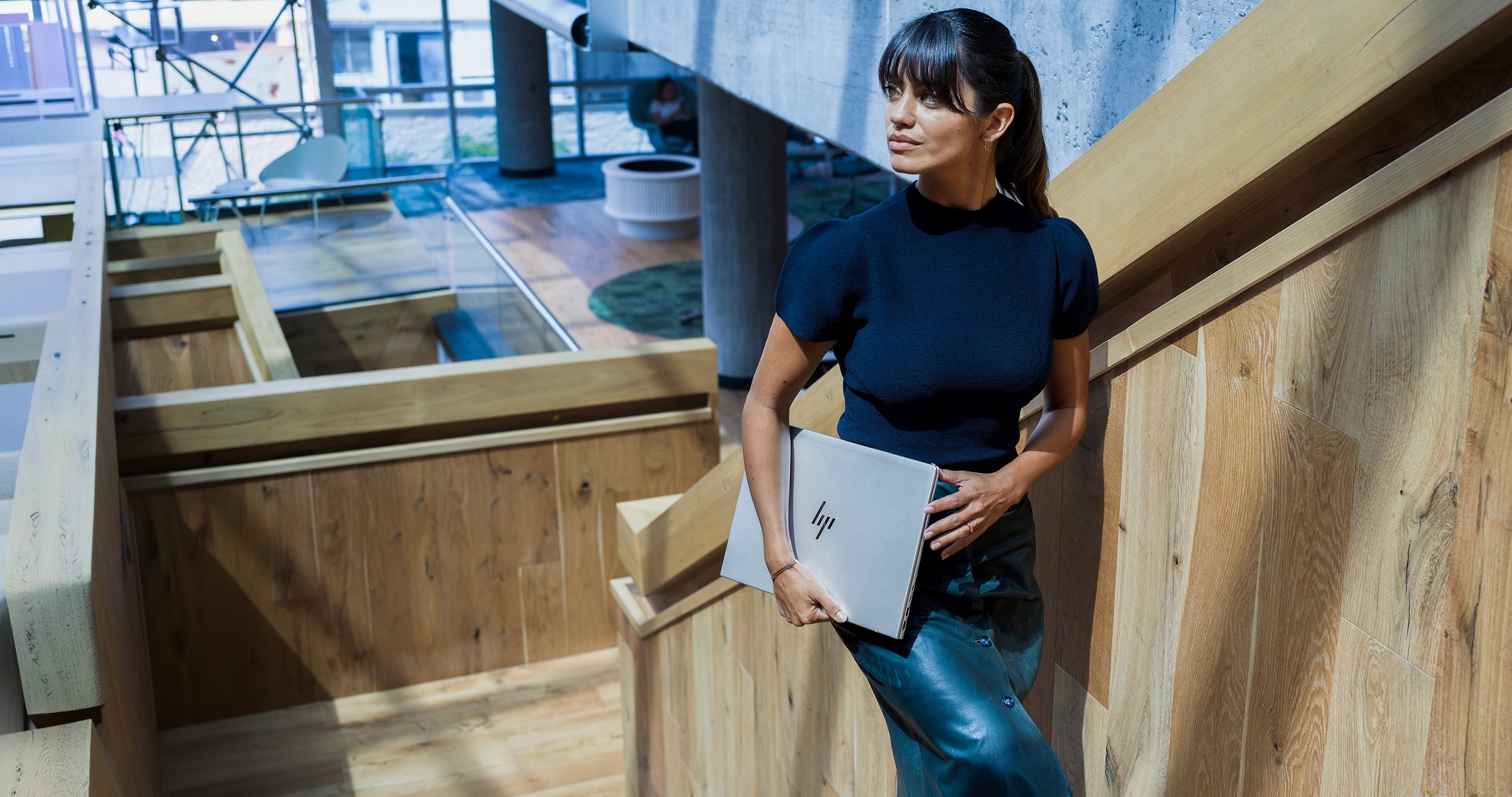 Woman walking up wooden stairs and carrying a silver HP laptop.