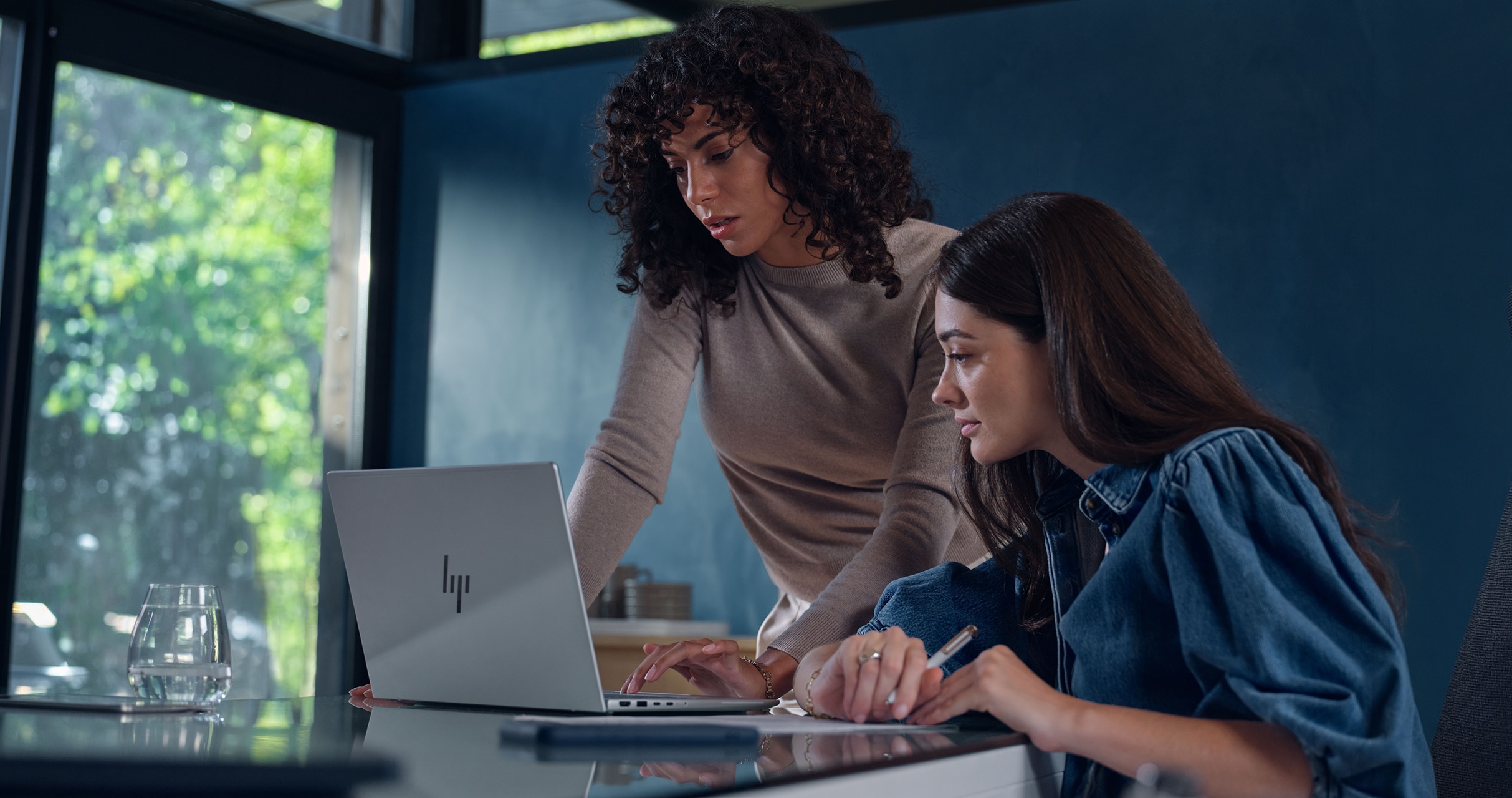 Two women collaborating and working on an HP laptop indoors.