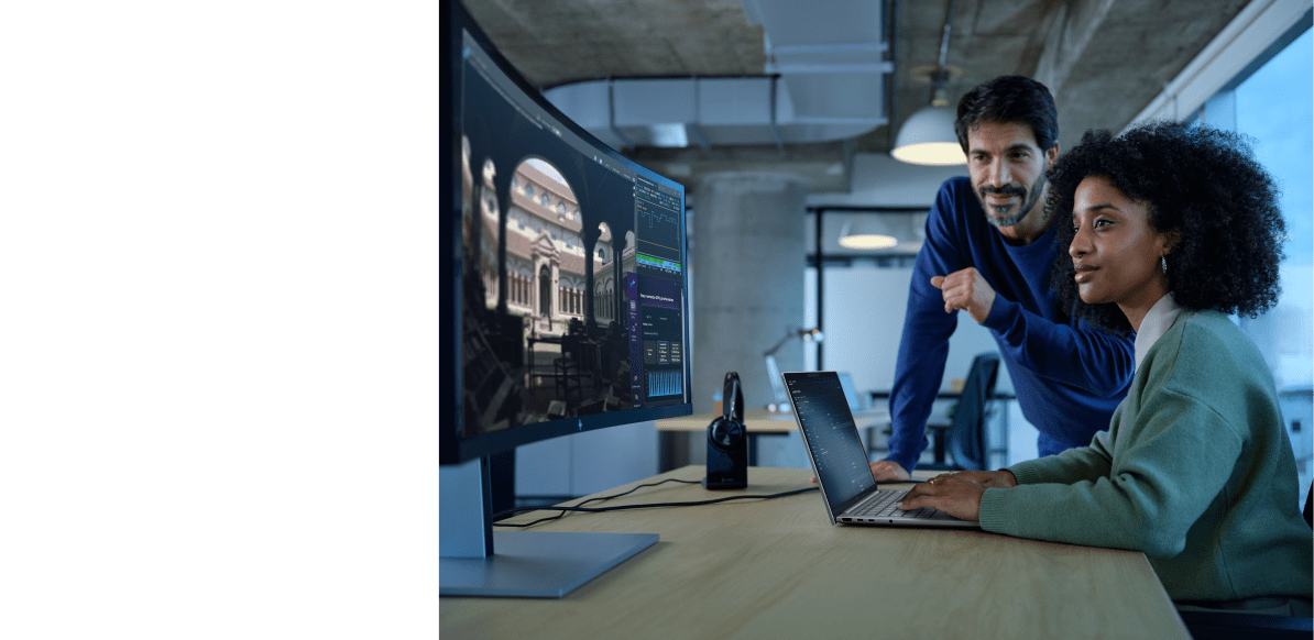 Woman on a laptop and looking at an external monitor with a coworker.