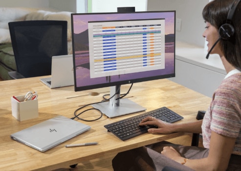 Una mujer trabajando en su monitor HP conectado a una laptop HP sobre un escritorio.