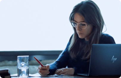 Eine Frau schreibt auf einem Zettel neben ihrem HP Laptop auf dem Schreibtisch.