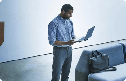 Ein Mann steht neben einem blauen Sofa und arbeitet auf seinem HP Notebook.