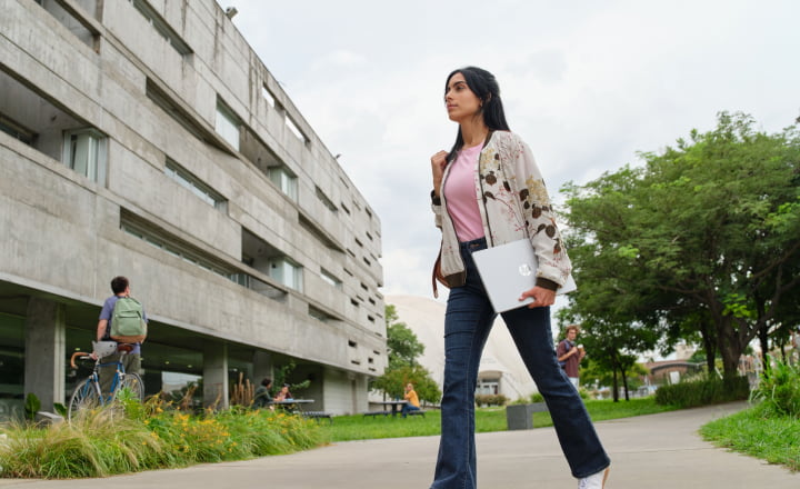 Young woman walking towards a class while carrying an HP OmniBook 5 Laptop AI PC