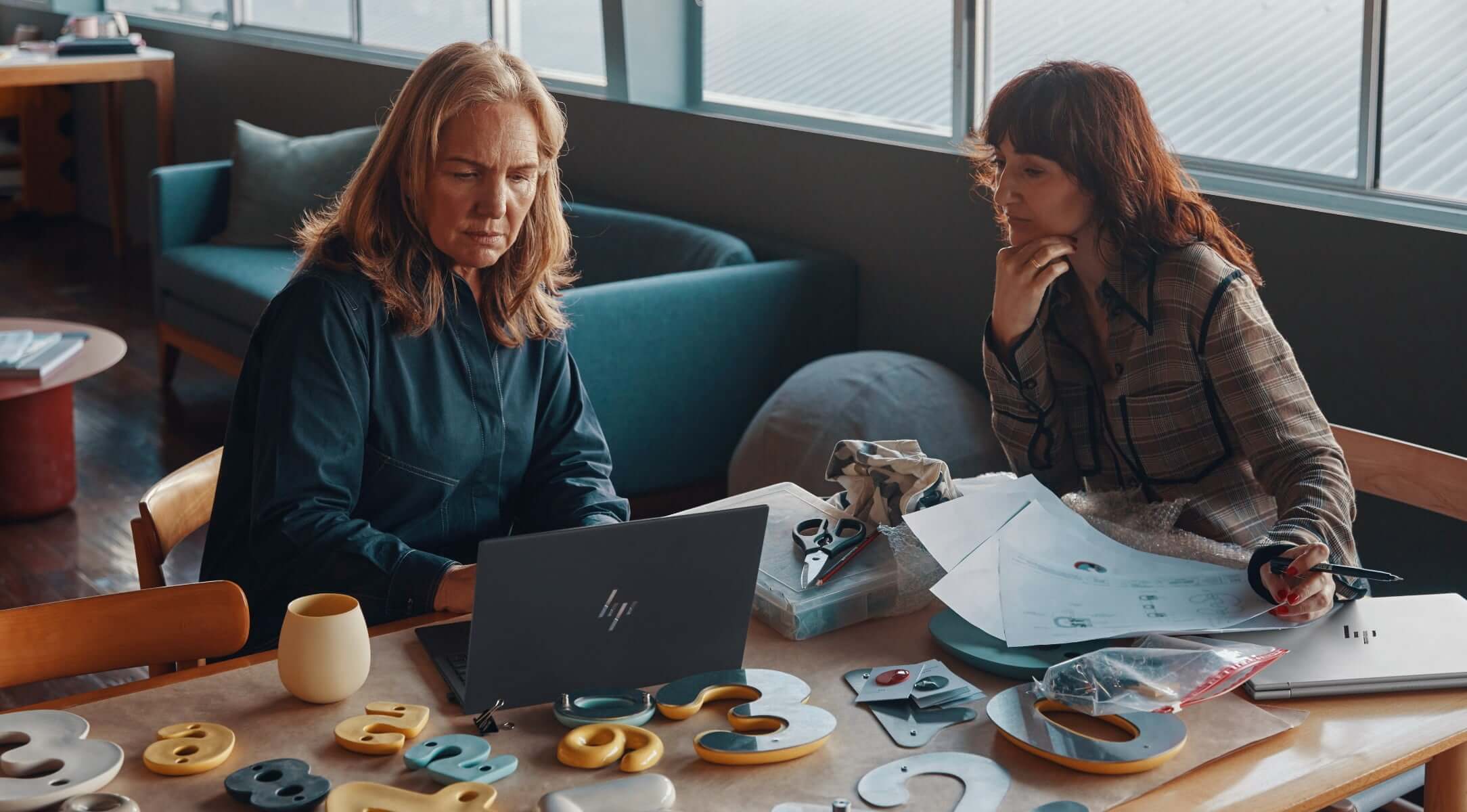 Two women working with some wooden models and looking at an HP laptop.