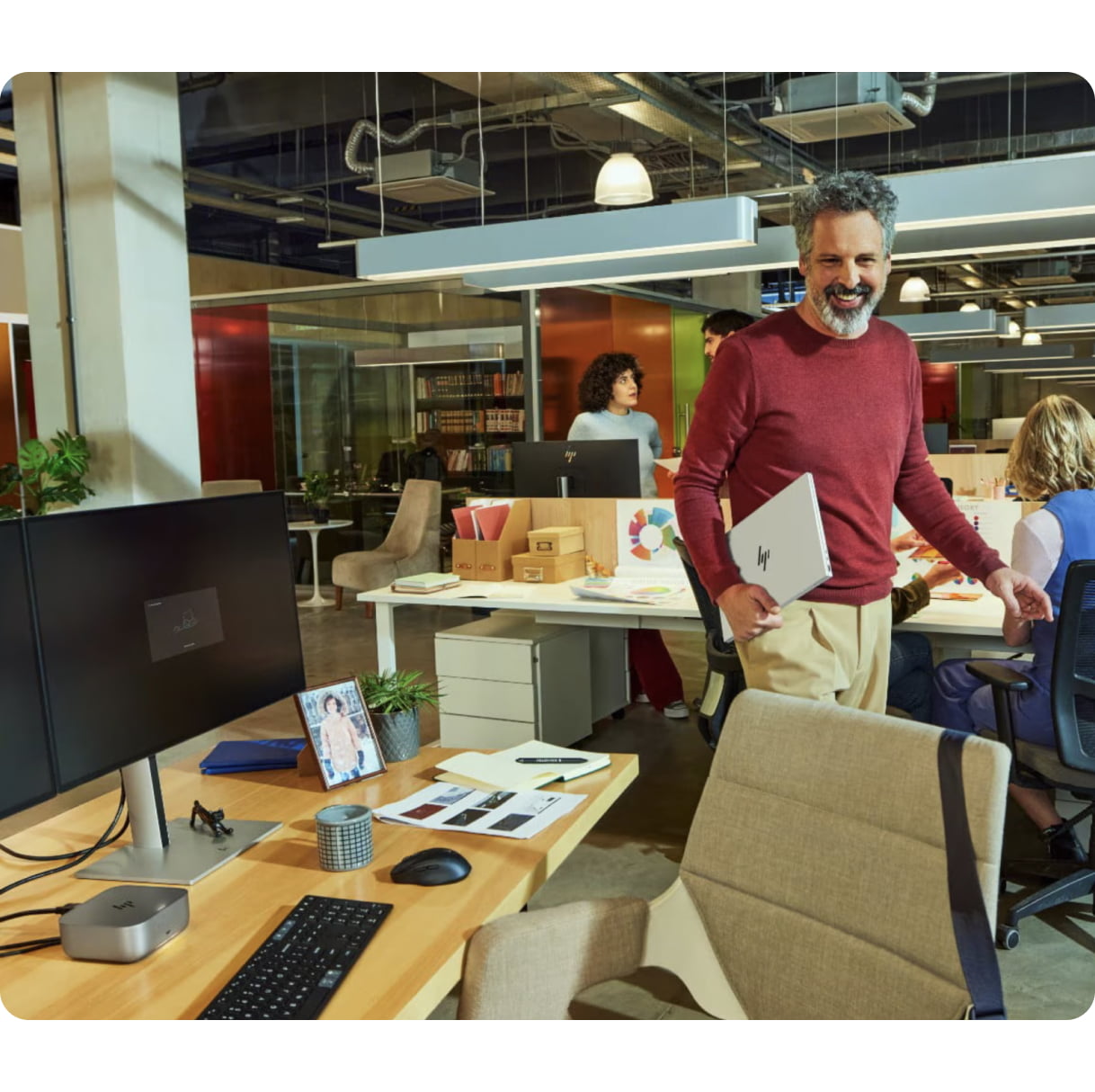Person holding an HP laptop and walking back to their desk in an office environment.
