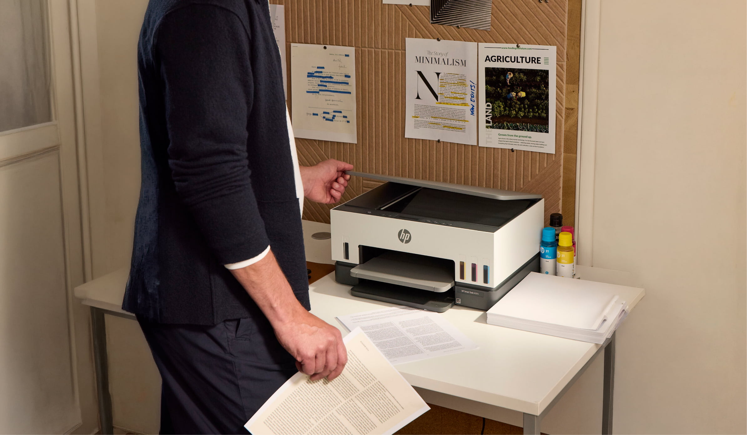 HP Smart Tank printer on desk with printed pages and ink bottles nearby.