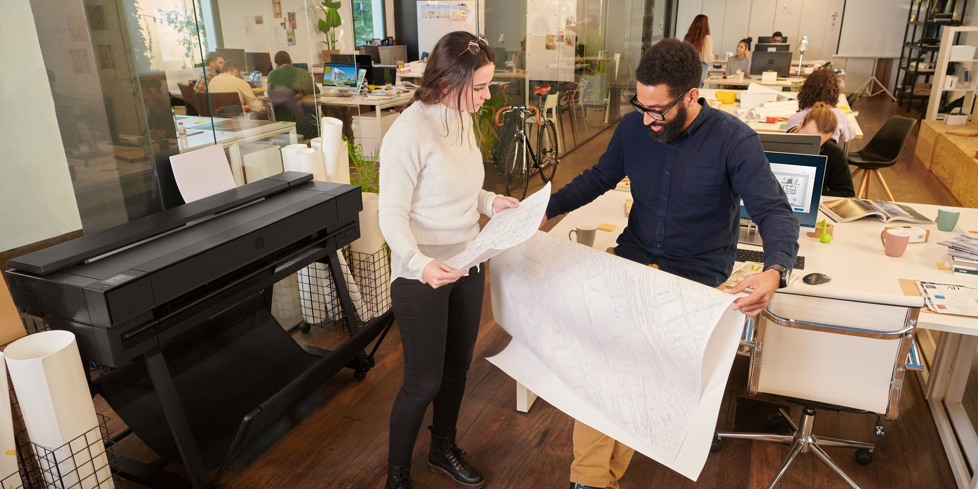 People checking prints in front of an HP DesignJet plotter in an office
