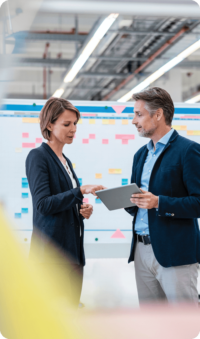 Two colleagues discussing work while reviewing a tablet in an office space.