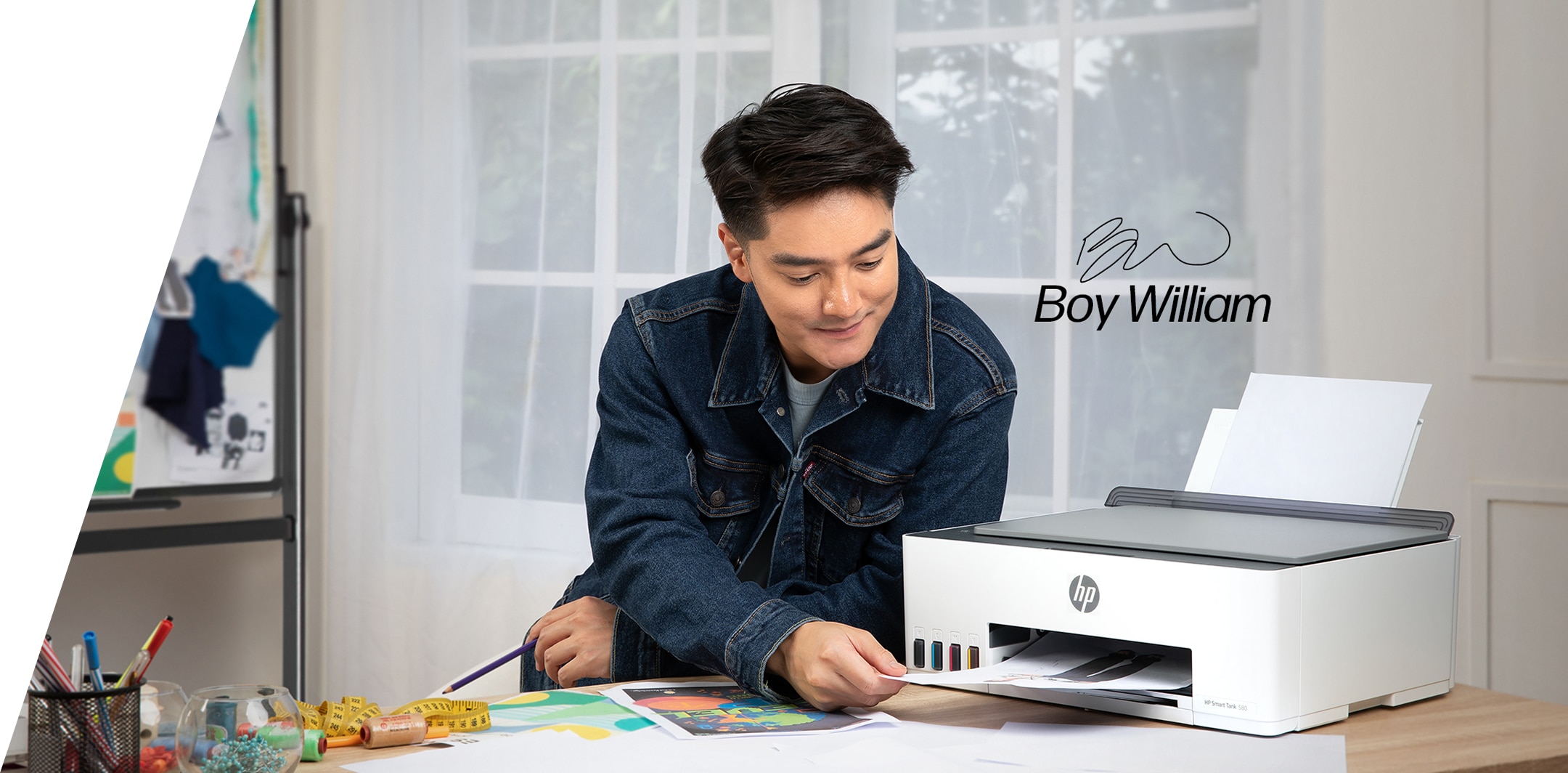 A wall with a shelf and a cabinet. An HP printer, toner cartridges, and printing paper are displayed on the cabinet, next to a photo frame. On the shelf are flowers, candlesticks, lamps, and photo frames.