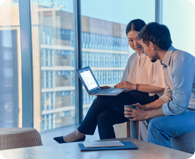 两个人正在靠近窗户的桌子上用笔记本电脑工作。