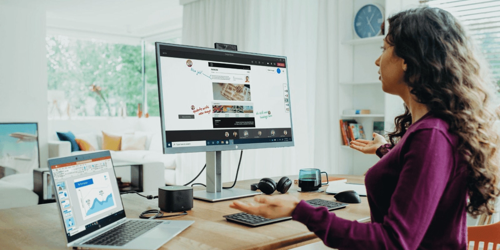 A woman sitting at a wooden desk talking into an HP monitor with a video call on the screen with an HP laptop with a PowerPoint presentation next to it. 