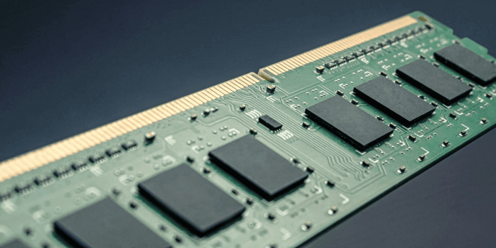 A close-up view of a computer RAM module shows the green circuit board with black memory chips and gold connectors against a dark background.