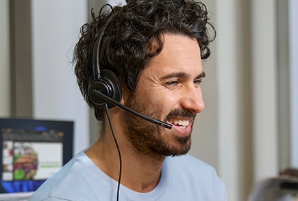 A person in a light blue shirt using poly wired headphones in an office