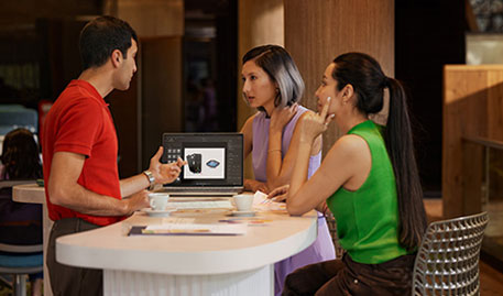 Three people talking around a table with an HP laptop showing a product.