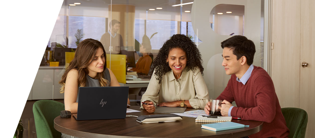 Three colleagues collaborate around a table with a laptop, documents, and notebooks.