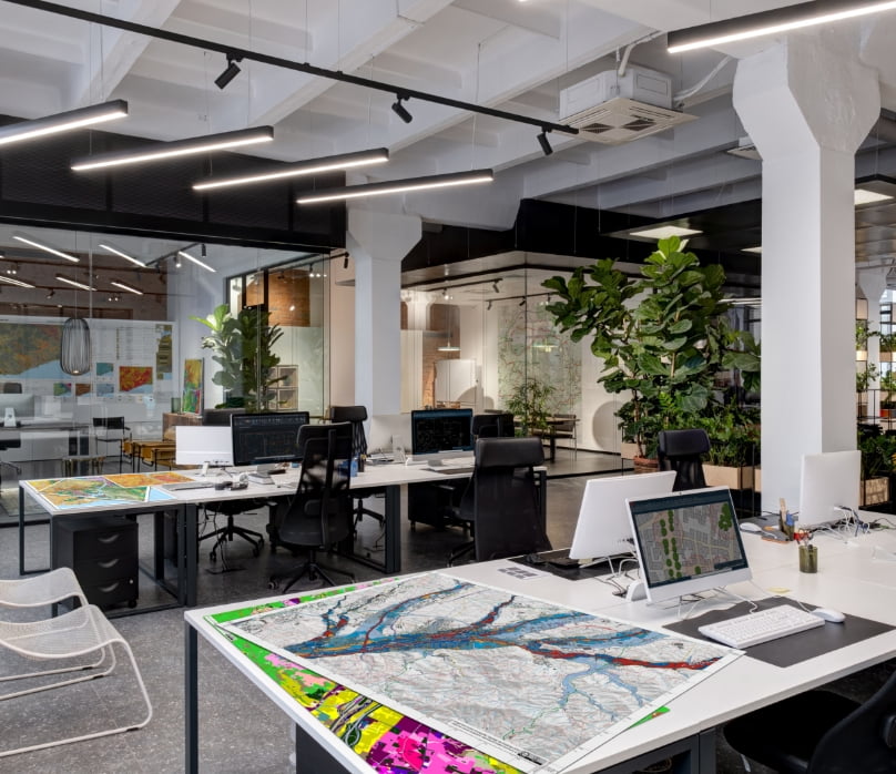 Planos SIG repartidos por mesas de trabajo en una oficina Planos SIG repartidos por mesas de trabajo en una oficina